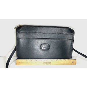 May include: Black leather crossbody bag with a top zipper closure and a front pocket. The bag features a logo on the front and a long strap. The bag measures approximately 12 inches wide.