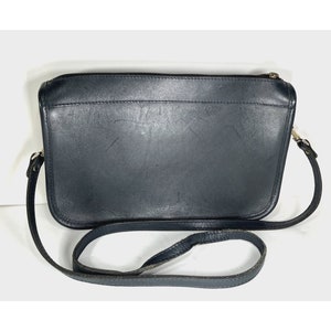 May include: A black leather crossbody bag with a long strap. The bag has a rectangular shape with a zipper closure and silver-toned hardware. The leather shows signs of wear.