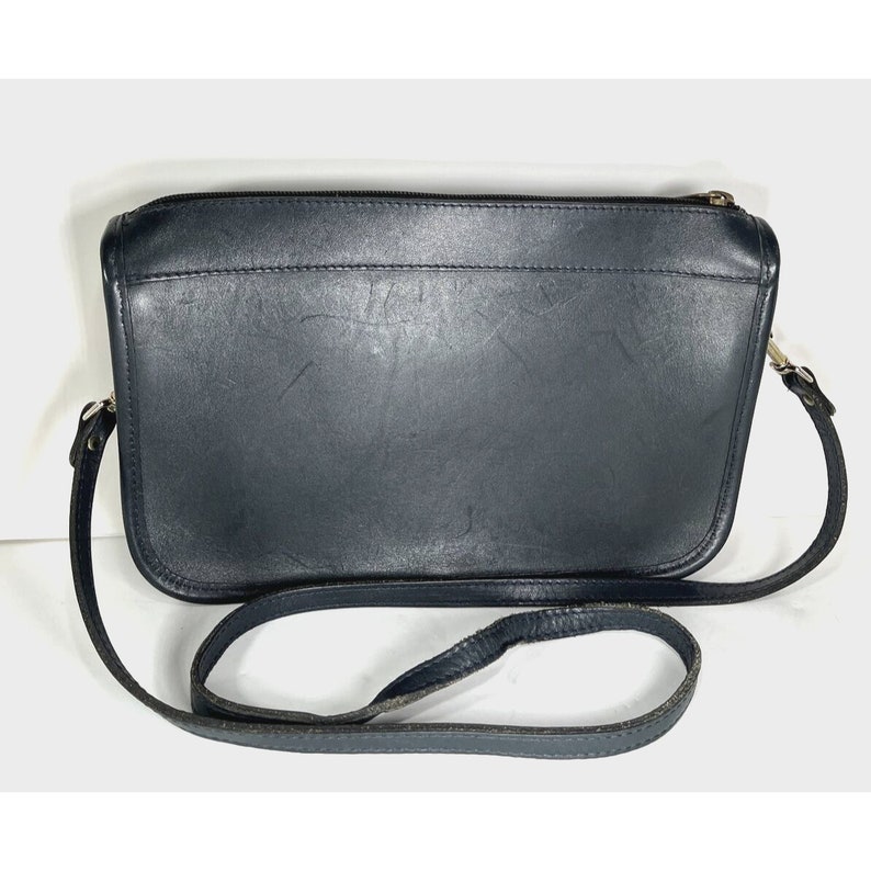 May include: A black leather crossbody bag with a long strap. The bag has a rectangular shape with a zipper closure and silver-toned hardware. The leather shows signs of wear.