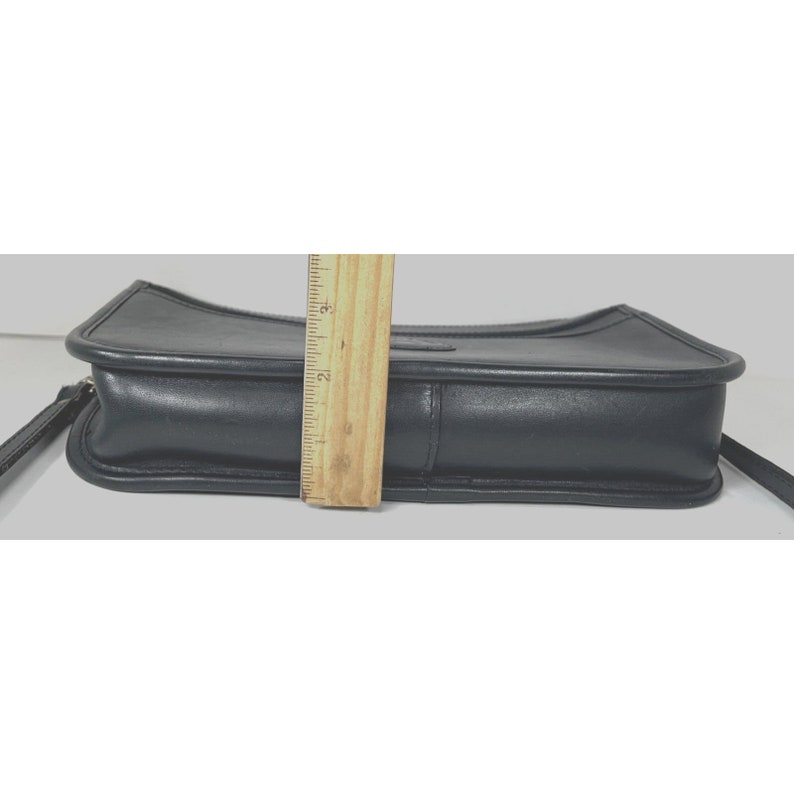 May include: A black leather crossbody bag with a rectangular shape. The bag has a top flap and a long strap. The bag's height is approximately 3 inches.
