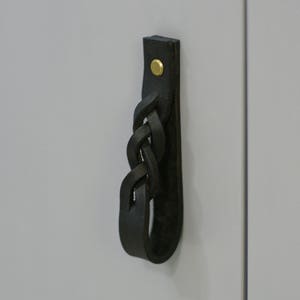 May include: Black leather cabinet pull with a braided design and a gold metal screw.