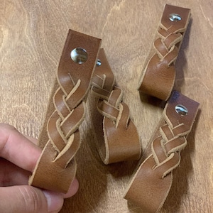 Puede incluir: Cuatro tiradores de cajón trenzados de cuero marrón con detalles metálicos plateados.