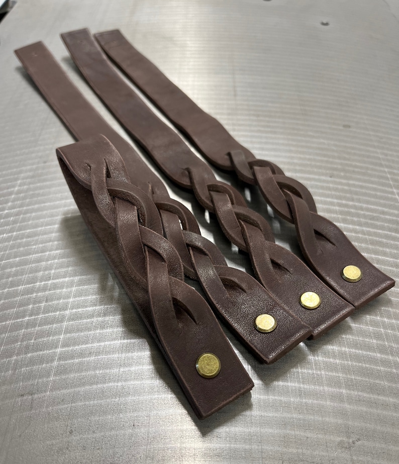 May include: Three brown leather braided straps with brass rivets. The straps are woven together in a complex pattern.