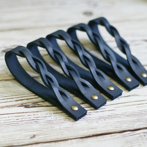 May include: Five dark blue leather braided handles with brass rivets. The handles are arranged in a row on a white wooden surface.