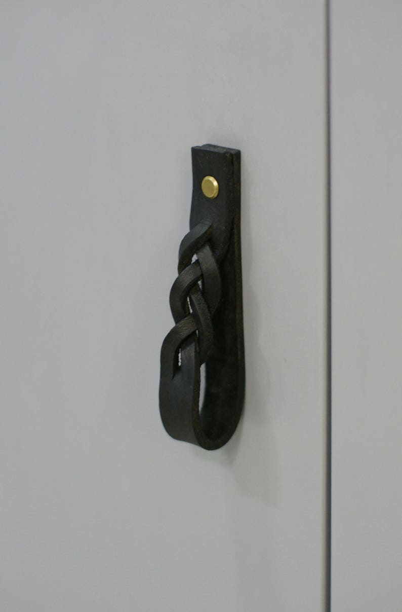 May include: Black leather cabinet pull with a braided design and a gold metal screw.