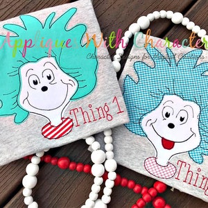 May include: Two gray t-shirts with embroidered images of Thing 1 and Thing 2 from the book "The Cat in the Hat". The shirts have the text "Thing 1" and "Thing 2" embroidered on them.