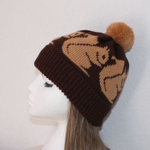 May include: Brown knitted beanie with a brown pom pom on top. The beanie has a tan pattern of stylised squirrels on it.