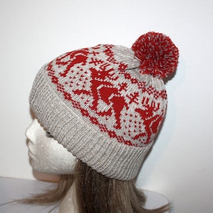 May include: A gray and red knitted beanie with a pom-pom on top. The beanie has a fair isle pattern with red reindeer on a gray background.