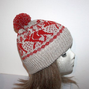 May include: A knitted winter hat with a red and white pattern featuring reindeer and snowflakes. The hat has a ribbed brim and a red pom-pom on top. The hat is displayed on a mannequin head.