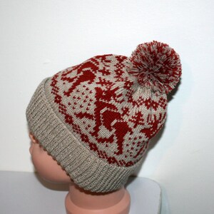 May include: A knitted winter hat with a red and beige reindeer pattern and a matching pom-pom. The hat has a ribbed brim and a fair isle design. This warm hat is perfect for cold weather.