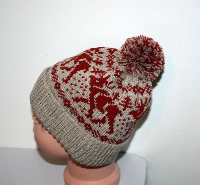May include: A knitted winter hat with a red and beige reindeer pattern and a matching pom-pom. The hat has a ribbed brim and a fair isle design. This warm hat is perfect for cold weather.