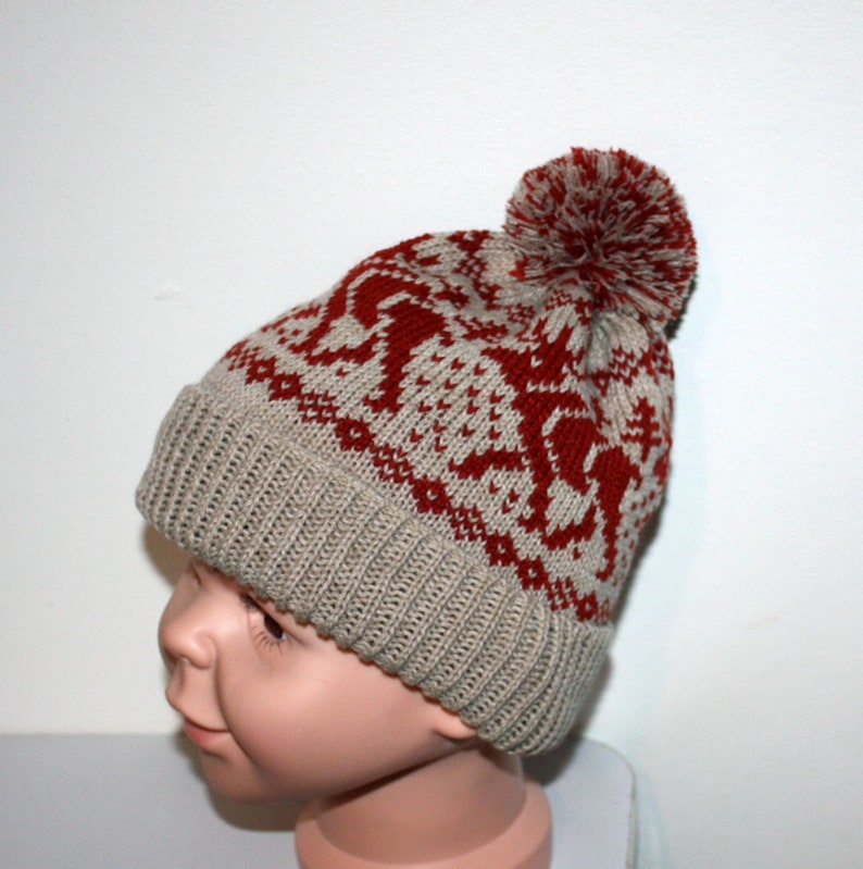 May include: A knitted winter hat with a red and beige pattern and a matching pom-pom. The hat features a ribbed brim and a repeating design. The hat is designed to keep the head warm during cold weather.