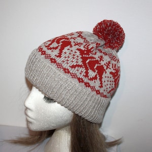 May include: A knitted winter hat with a red and white pattern and a red pom-pom. The hat is light gray with a ribbed brim and a repeating pattern of red shapes. The pom-pom is a solid red color.