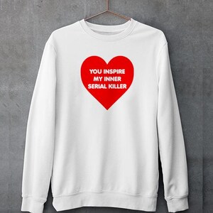 May include: White sweatshirt with a large red heart graphic. The heart contains the text "YOU INSPIRE MY INNER SERIAL KILLER" in white. The sweatshirt is hanging on a metal hanger.