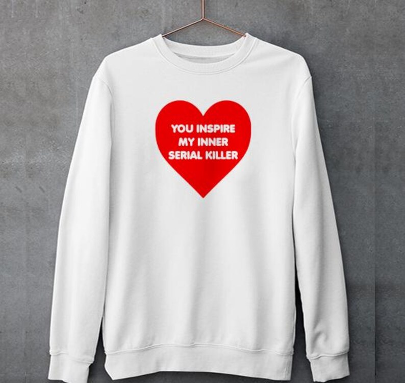 May include: White sweatshirt with a large red heart graphic. The heart contains the text "YOU INSPIRE MY INNER SERIAL KILLER" in white. The sweatshirt is hanging on a metal hanger.
