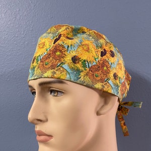 May include: A yellow, blue, and brown patterned surgical scrub hat with a sunflower design. The hat has a tie at the back.