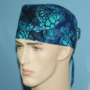 May include: A blue and teal surgical scrub hat with a pattern of sea turtles. The hat has a tie at the back.