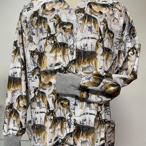 May include: A white scrub top with a grey trim and a repeating pattern of brown and black wolves on a white background.