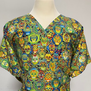 May include: A green, blue, and yellow scrub top with a V-neck and a pattern of colorful sugar skulls.
