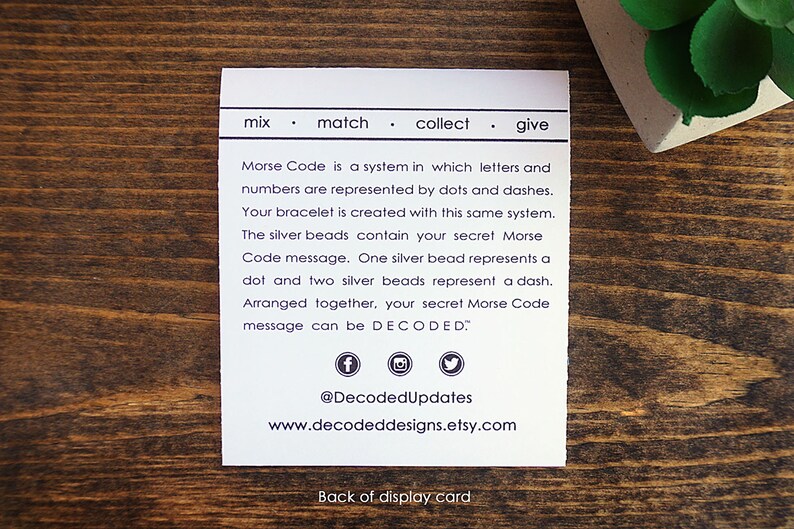 May include: White card with black text explaining how to decode a Morse code bracelet. The text reads "mix match collect give Morse Code is a system in which letters and numbers are represented by dots and dashes. Your bracelet is created with this same system. The silver beads contain your secret Morse Code message. One silver bead represents a dot and two silver beads represent a dash. Arranged together, your secret Morse Code message can be DECODED." The card also includes social media icons and the text "@DecodedUpdates www.decodeddesigns.etsy.com Back of display card."