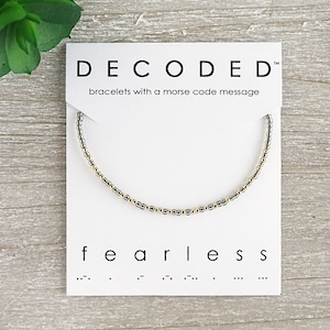 May include: A white card with the text "DECODED" and "bracelets with a morse code message". The card shows a silver and gold beaded bracelet with the word "fearless" and its morse code translation below.