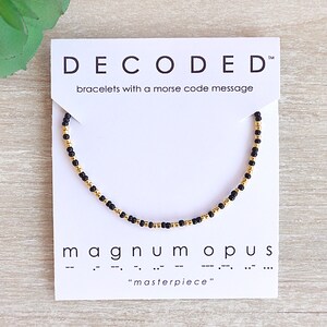 May include: Black and gold beaded bracelet with a card that reads "DECODED" bracelets with a morse code message "magnum opus" "masterpiece"