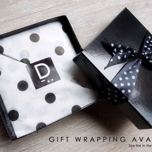 May include: A black gift box with a white polka dot ribbon. The box is open and the inside is lined with white tissue paper with black polka dots. The tissue paper has a black logo with the letter "D" on it.