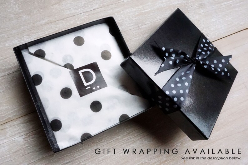 May include: A black gift box with a white polka dot ribbon. The box is open and the inside is lined with white tissue paper with black polka dots. The tissue paper has a black logo with the letter "D" on it.