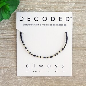 Peut inclure: Bracelet en perles noires et dorées avec le mot "always" et sa traduction en code Morse sur une carte blanche avec le nom de la marque "DECODED" et le texte "bracelets avec un message en code Morse".