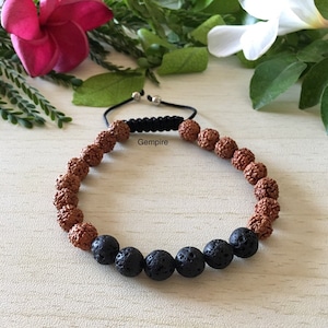 Może przedstawiać: Bransoletka z brązowych i czarnych koralików, z czarnym sznurkiem i srebrnym metalowym zapięciem. Bransoletka ma w środku część zawiązaną węzłem z nadrukowanym słowem "Gempire".