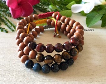 May include: A set of three beaded bracelets with a wooden base, red tiger's eye, gold tiger's eye, and blue tiger's eye beads. The bracelets are tied together with red, yellow, and gray cords.
