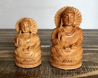 May include: Two wooden Buddha statues, one larger than the other, both with intricate carvings and a serene expression. The statues are sitting on a wooden surface.