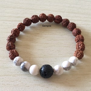 May include: A brown, white, and black beaded bracelet with a lava rock bead in the center. The bracelet is made of rudraksha beads, white howlite beads, and a black lava rock bead.