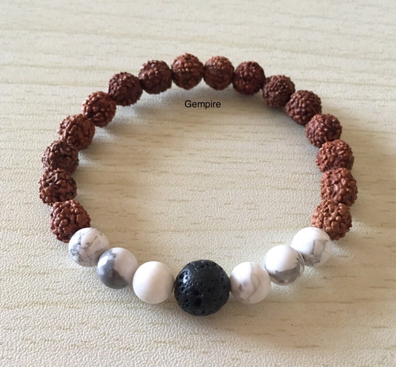 May include: A brown, white, and black beaded bracelet with a lava rock bead in the center. The bracelet is made of rudraksha beads, white howlite beads, and a black lava rock bead.