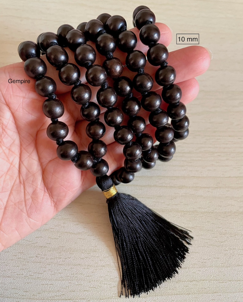 May include: A black wooden mala bead necklace with a black tassel. The beads are 10 mm in diameter. The necklace is 108 beads long. 10 mm.