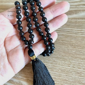 May include: Black wooden beaded necklace with a black tassel. The beads are 6 mm in diameter. Gemspire is written on the tag.