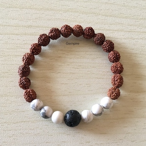 Può includere: Un braccialetto di perline marroni e bianche con un ciondolo di lava nera. Il braccialetto ha la scritta "Gemfire" stampata.