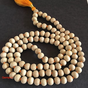 Pu&ograve; includere: Una collana mala in legno color chiaro con filo arancione e nappa gialla. Le perline sono lisce e cilindriche, infilate in pi&ugrave; fili. La collana viene probabilmente utilizzata per la meditazione o la preghiera.