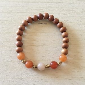 May include: A brown wooden beaded bracelet with three orange gemstone beads and one white gemstone bead. The bracelet has gold accents on the beads.
