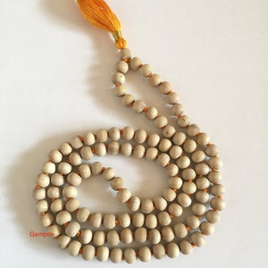 Pu&ograve; includere: Una collana di perline mala in legno di colore chiaro con filo arancione e un nappa gialla. Le perline sono lisce e rotonde, e la nappa &egrave; fatta di fili sottili. La collana viene probabilmente utilizzata per la meditazione o pratiche spirituali.