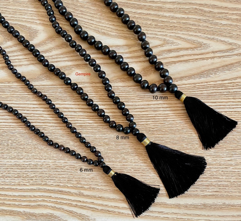 May include: Three black wooden bead necklaces with tassels. The necklaces are 6 mm, 8 mm, and 10 mm in diameter.