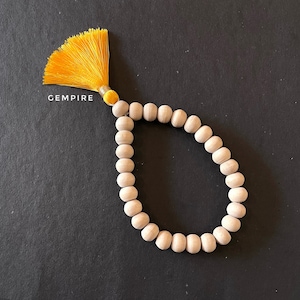 May include: A wooden beaded bracelet with a yellow tassel. The bracelet is made of natural wood beads and has a simple, elegant design.