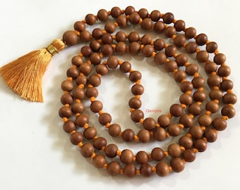 May include: A brown wooden mala bead necklace with a tassel. The beads are strung on a thin orange cord. The tassel is made of orange thread.