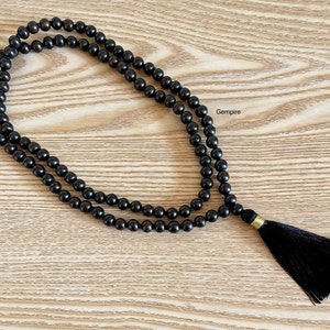 May include: A black wooden mala bead necklace with a black tassel. The necklace is made of 108 beads and is approximately 18 inches long.