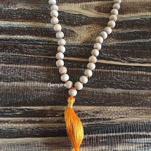 Pu&ograve; includere: Una collana di perline con perline di legno di colore chiaro infilate su un filo arancione. La collana ha una nappa arancione brillante all'estremit&agrave;. La parola "Gempire" &egrave; stampata sull'immagine.