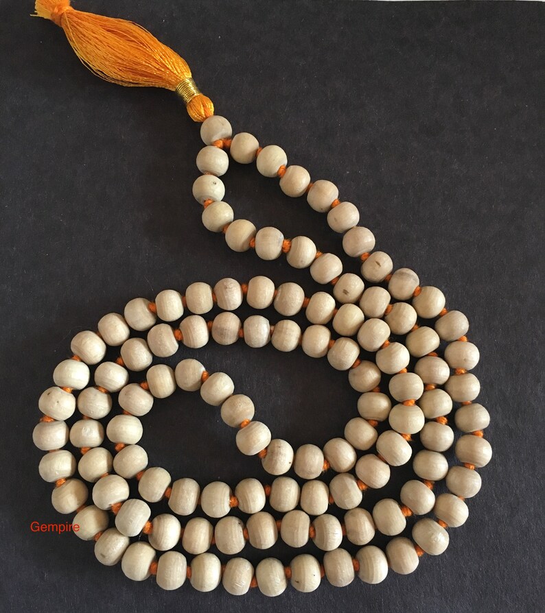 Pu&ograve; includere: Una collana di perline di legno color chiaro con un nappa e un filo arancione. Le perline sono di forma ovale e infilate con filo arancione. La nappa &egrave; fatta di fili arancioni e filo dorato.