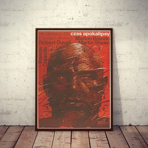 May include: A vintage movie poster for the film "Apocalypse Now" featuring a close-up of Marlon Brando's face. The poster is red and brown with the text "Czas Apokalipsy" in Polish.