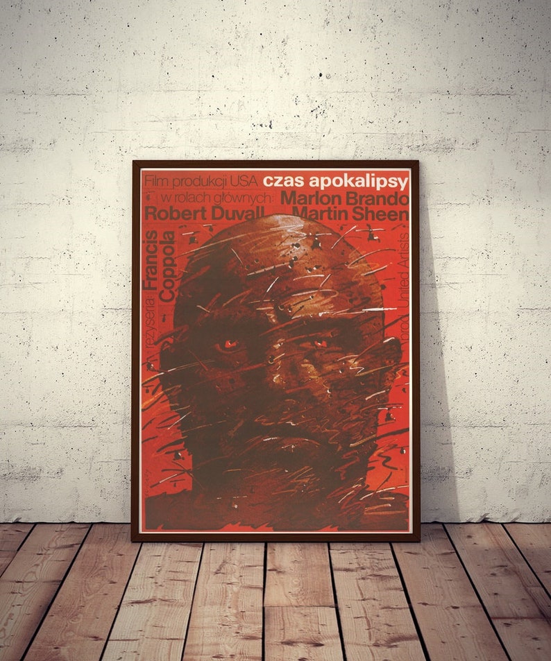 May include: A vintage movie poster for the film "Apocalypse Now" featuring a close-up of Marlon Brando's face. The poster is red and brown with the text "Czas Apokalipsy" in Polish.