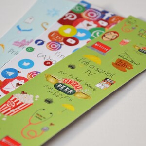 Può includere: Quattro strisce di segnalibro verdi con vari adesivi colorati. Gli adesivi presentano loghi di piattaforme di social media, programmi televisivi e altri riferimenti della cultura popolare. Il testo sui segnalibri recita "Sono una serie TV" e "Il posto dove gli amici si incontrano".
