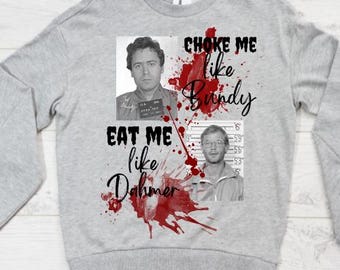 May include: A light gray sweatshirt featuring two black and white mugshot images. The text "CHOKE ME like Bundy" and "EAT ME like Dahmer" is written in black script with red blood splatter accents.